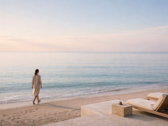Woman walking barefoot along a calm shoreline at dawn, with soft light over the sea and a quiet coastal terrace in the foreground.