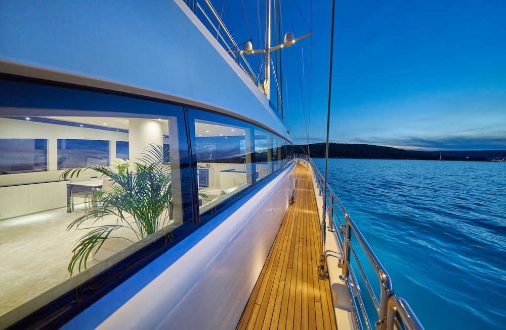 Acapella yacht side deck in the evening with illuminated interior and sea views