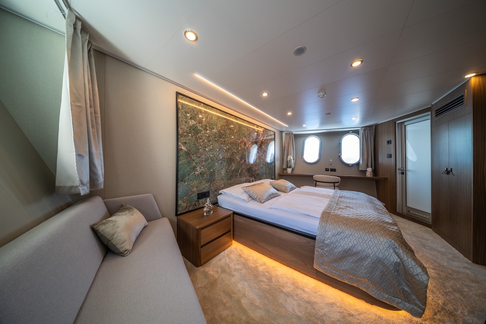 Master cabin on Olimp yacht with warm wood finishes, soft lighting, and sea-view windows