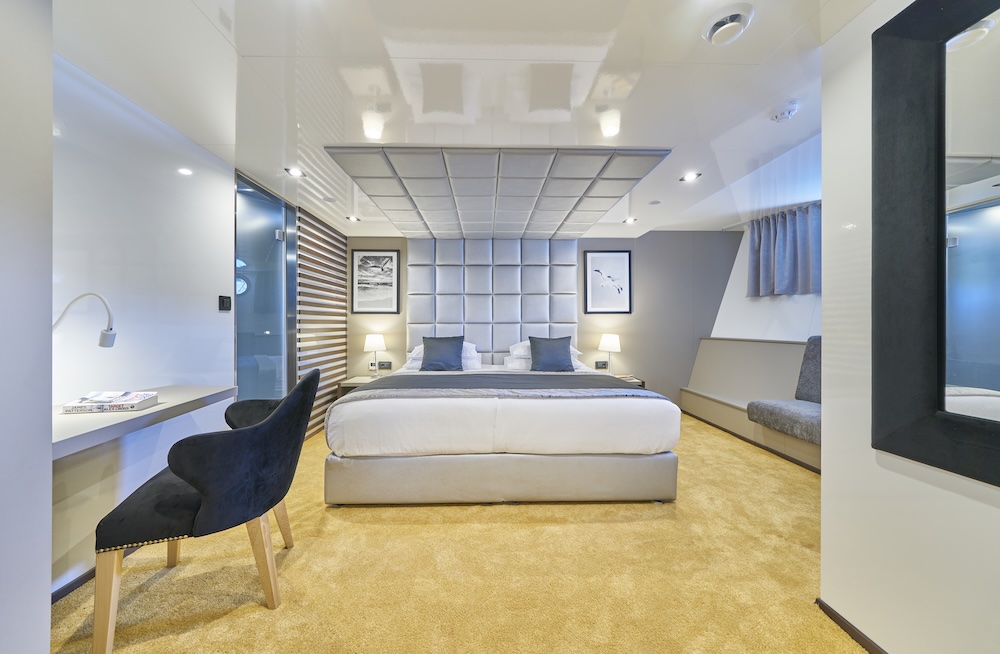 Bright master cabin with upholstered headboard, desk area, and soft lighting on Rara Avis yacht