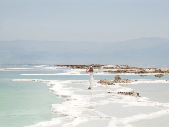 Woman walking along white mineral salt formations at the Dead Sea under a clear blue sky