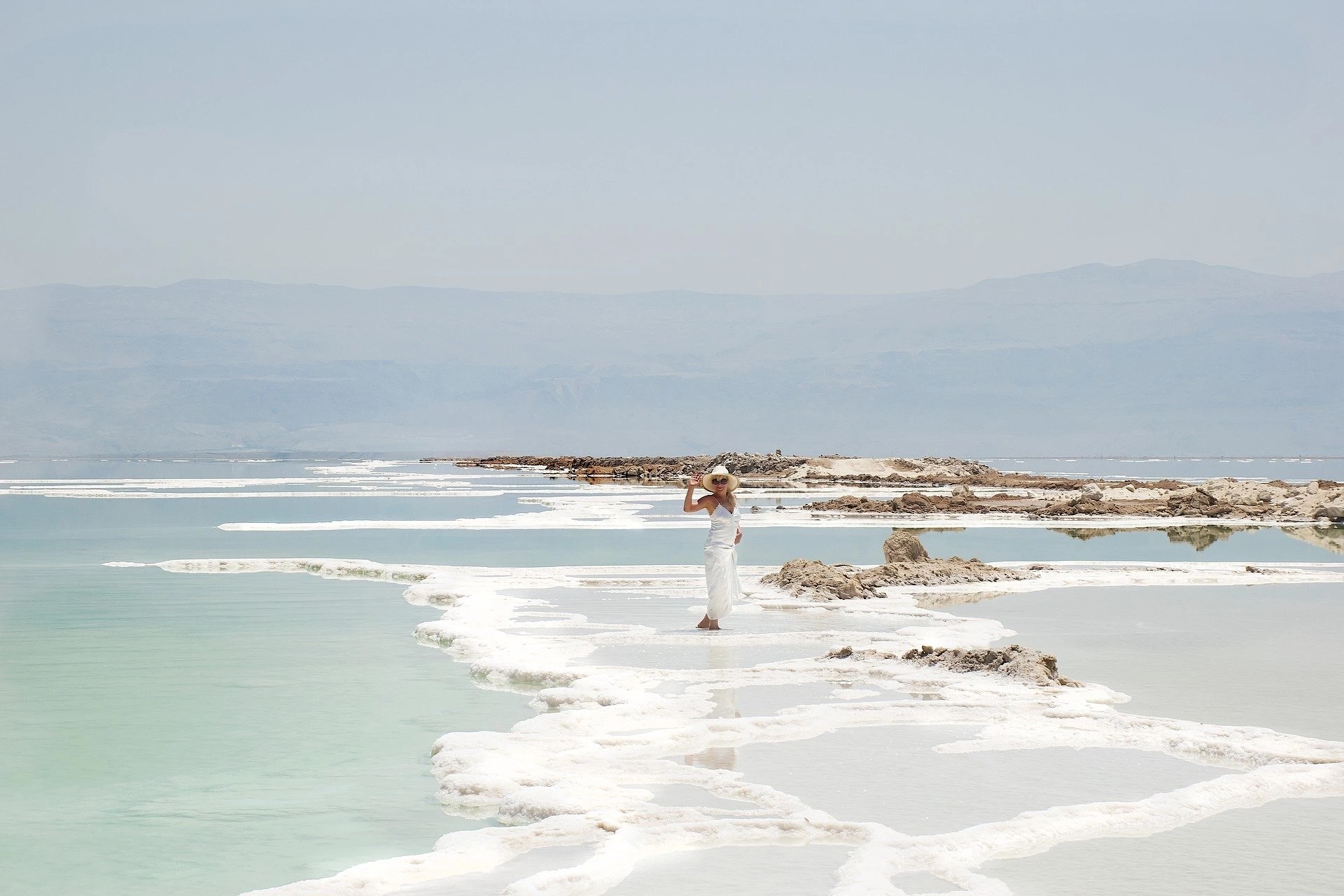 Woman walking along white mineral salt formations at the Dead Sea under a clear blue sky