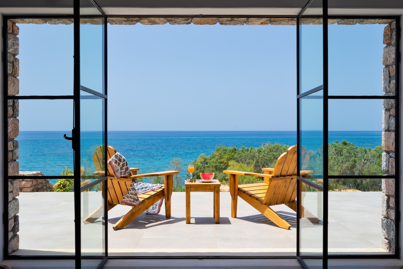 Open black-framed glass doors overlooking two timber chairs and the Libyan Sea in Crete