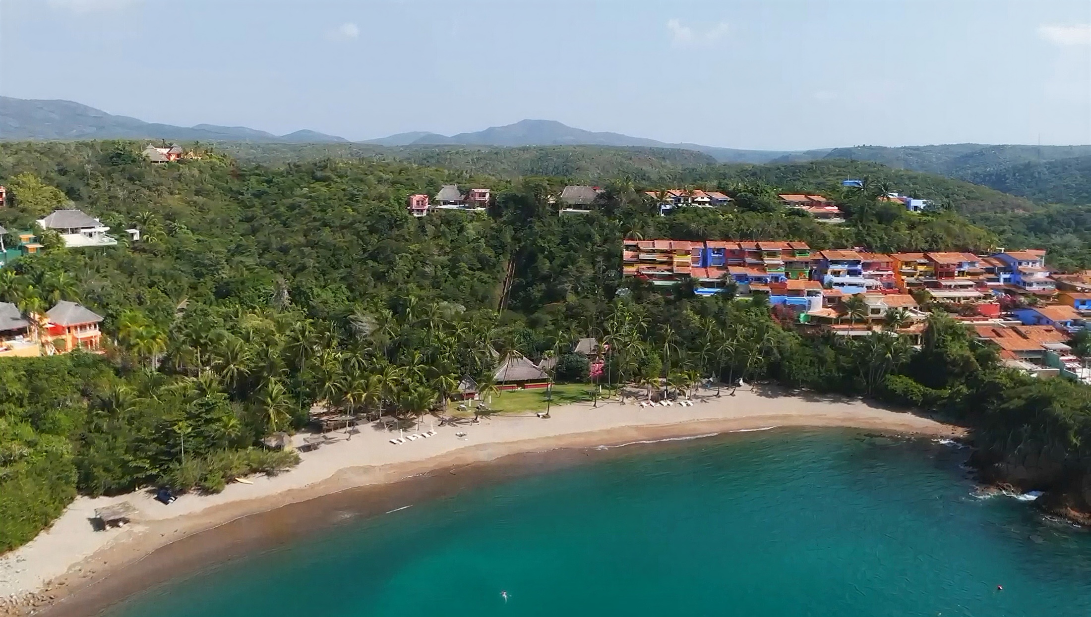Aerial view of colourful hillside residences overlooking a palm-lined bay in Careyes, Mexico