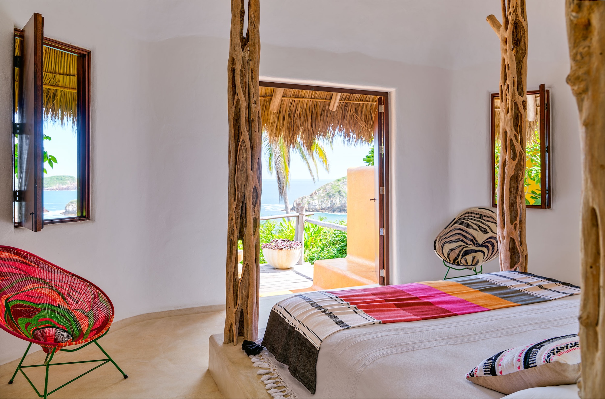 Ocean-view suite at Casa Torre with a king-size bed, sculptural timber bedposts, woven chairs and a private terrace overlooking the Pacific.
