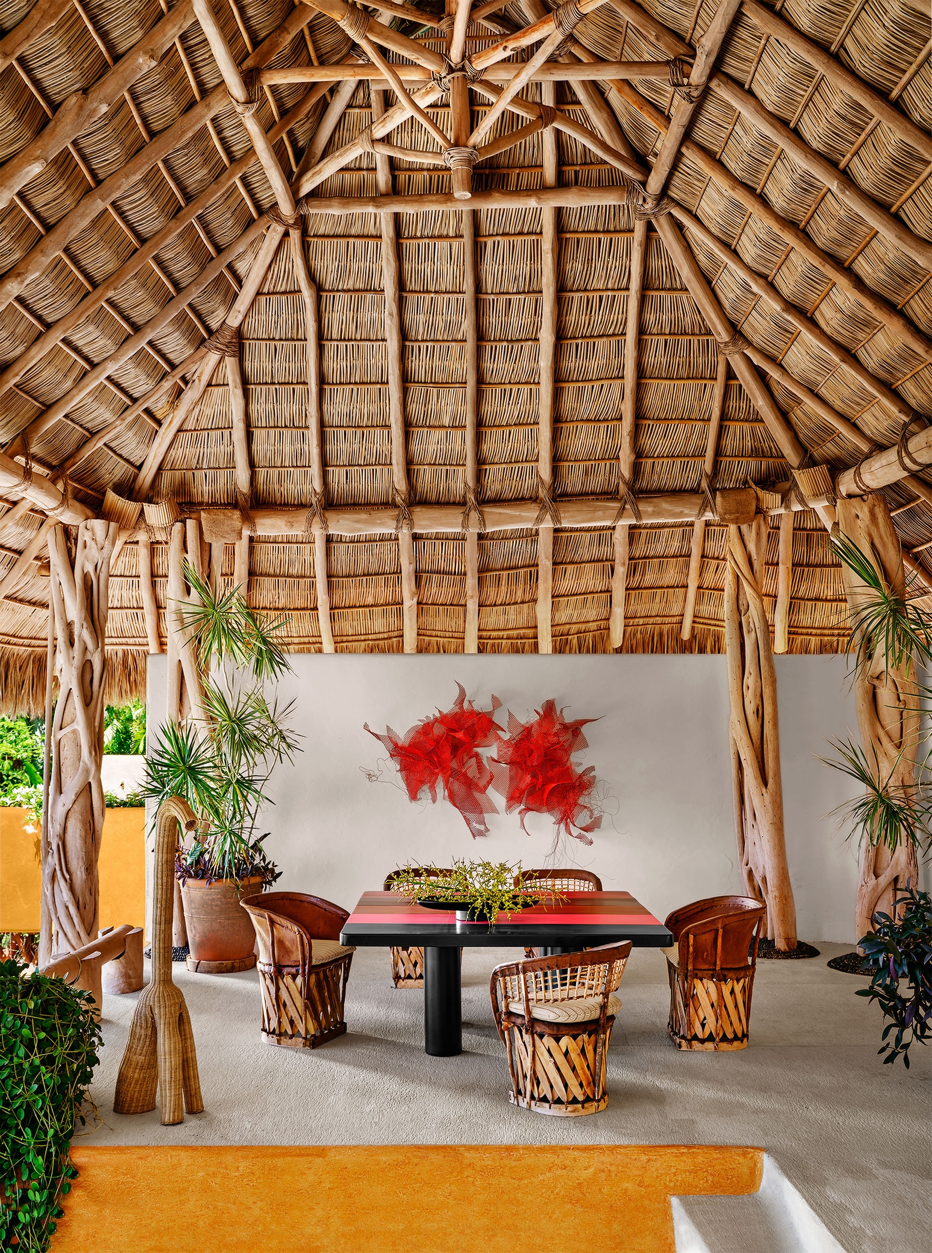 Open-air dining area at Casa Torre beneath a high thatched palapa roof with timber columns, woven chairs and contemporary artwork.