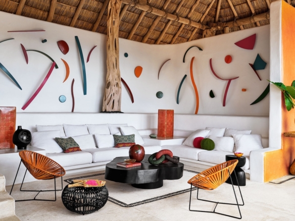 Mexican living room with white built-in seating, colourful art and woven palapa roof