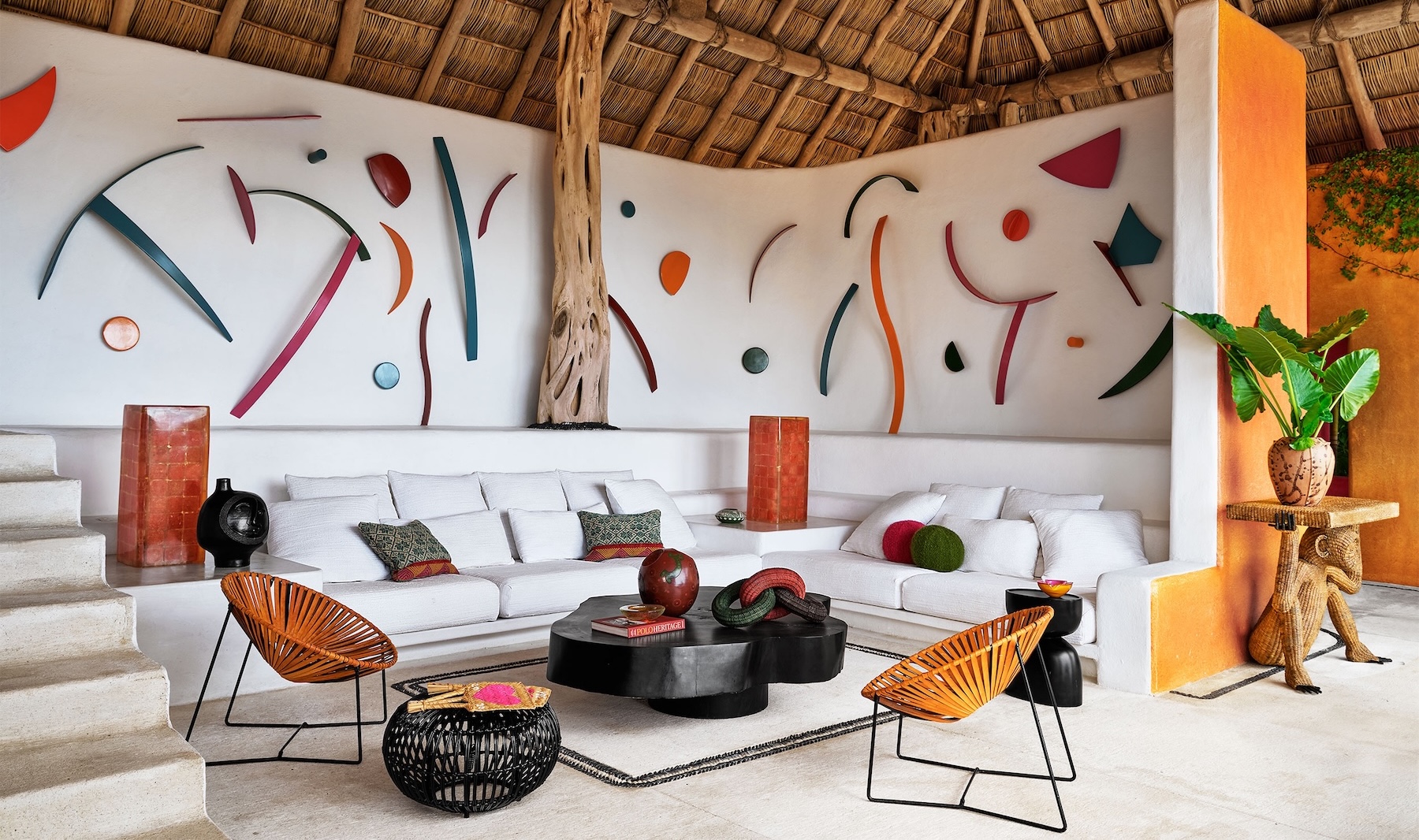 Mexican living room with white built-in seating, colourful art and woven palapa roof