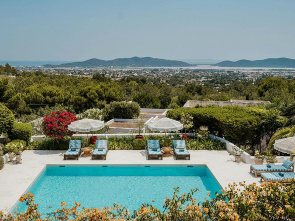 Swimming pool and striped loungers surrounded by gardens at El Zafiro villa in Ibiza, with distant sea views