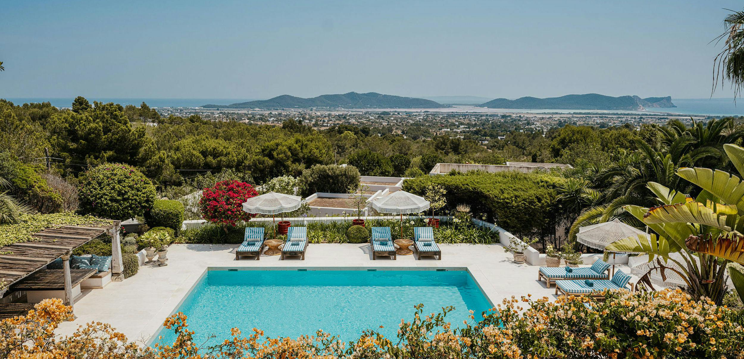 Swimming pool and striped loungers surrounded by gardens at El Zafiro villa in Ibiza, with distant sea views