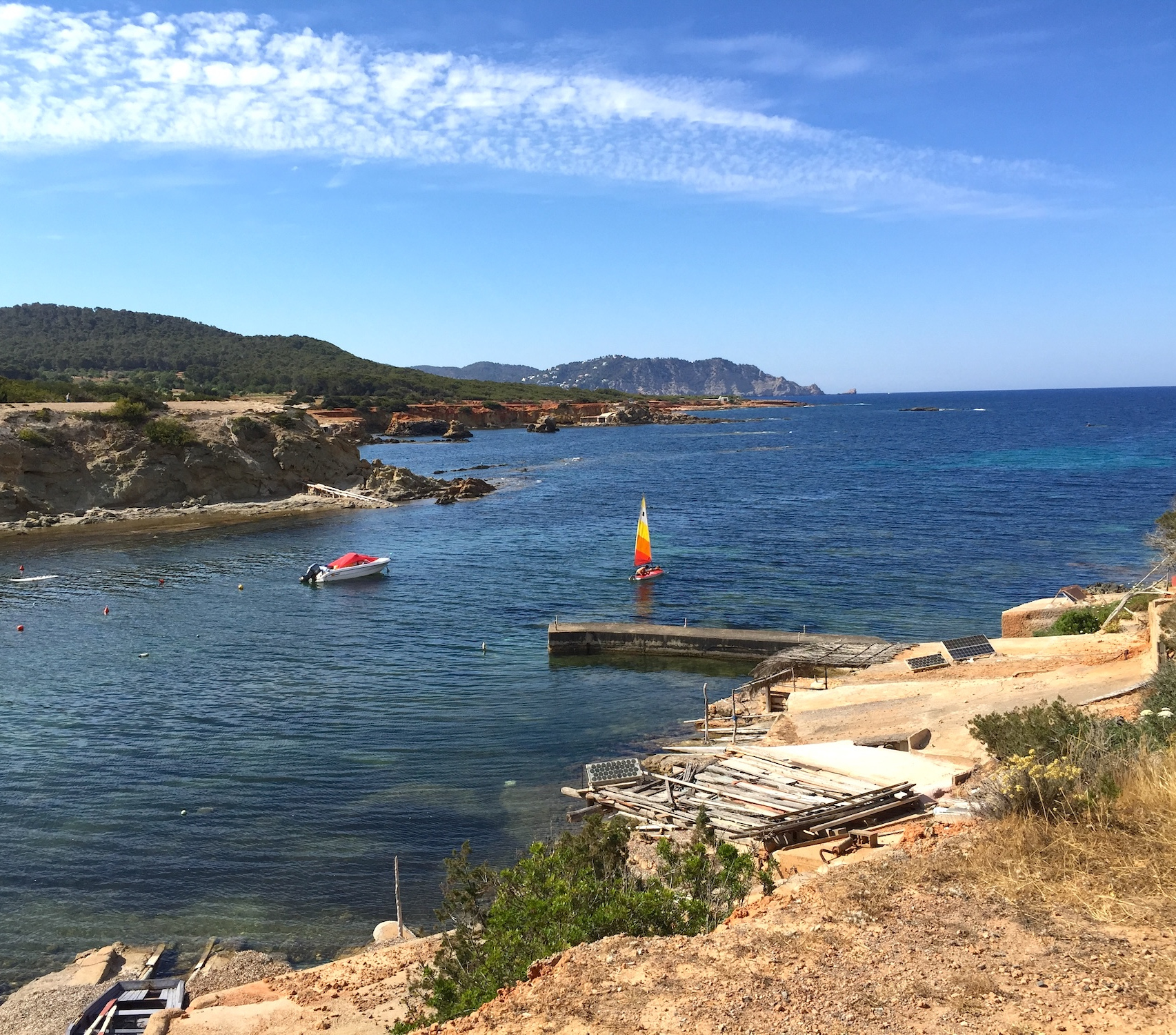 Small sailing boat with a colorful sail on the Mediterranean Sea beside a rocky coastline in Ibiza