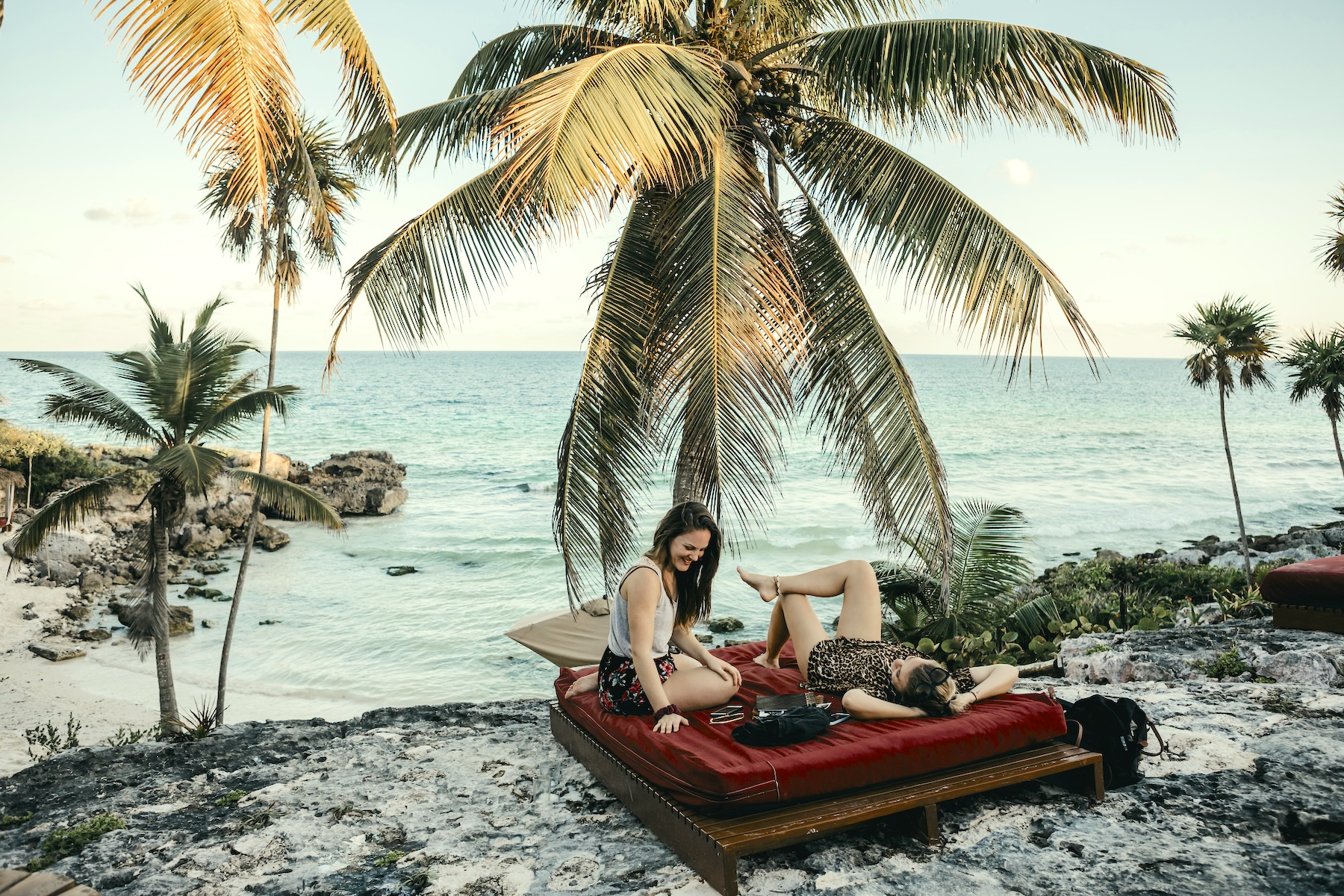 Two women relaxing beneath palm trees overlooking the Caribbean coast in Tulum, Mexico.
