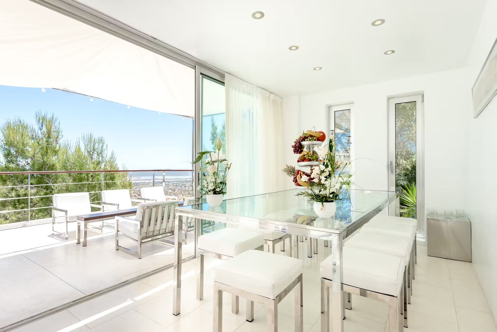 Light-filled dining area at Villa Destiny Ibiza, with a glass dining table and sliding doors opening onto a furnished terrace.