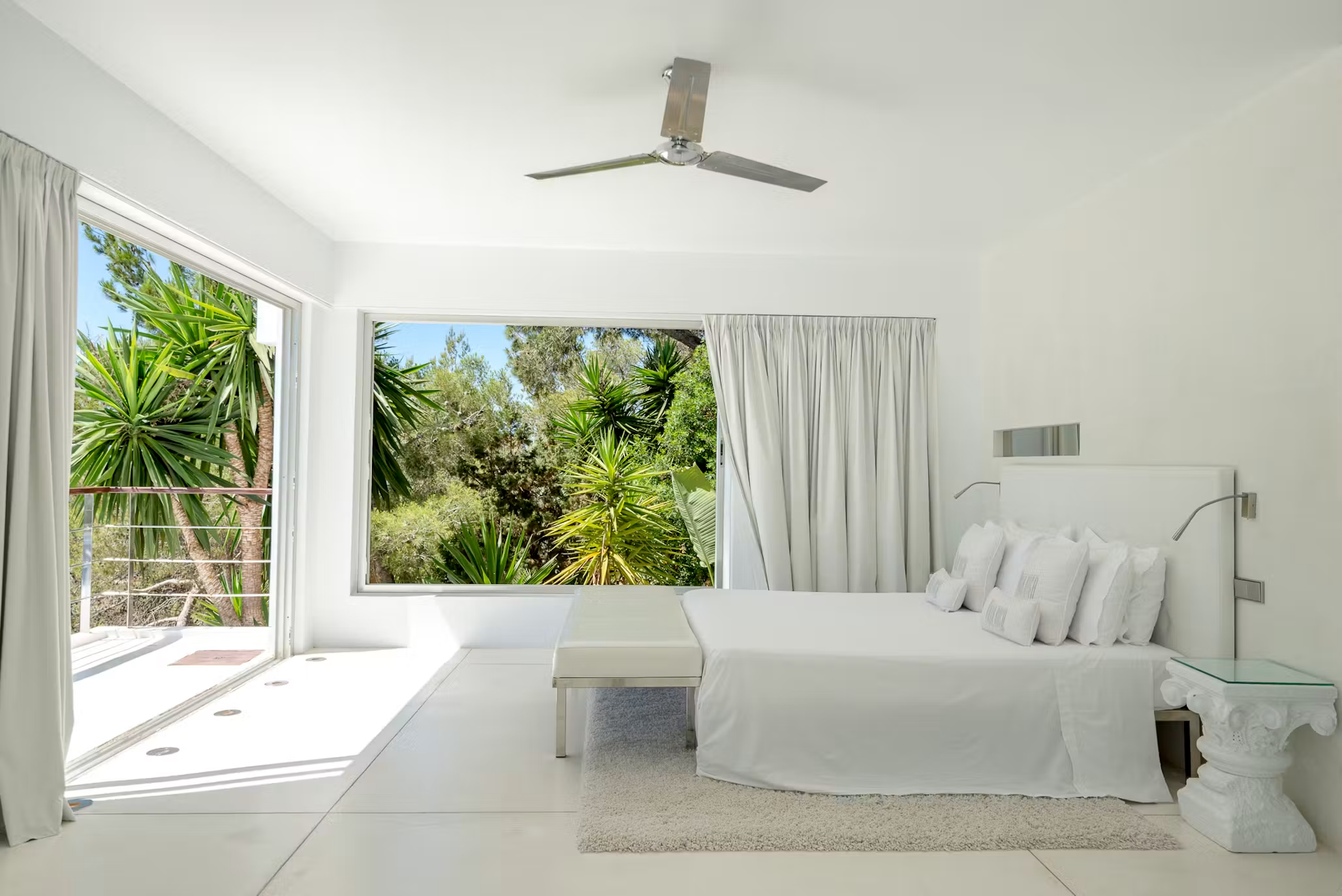 White bedroom at Villa Destiny Ibiza with large windows overlooking surrounding greenery and a door to the outside