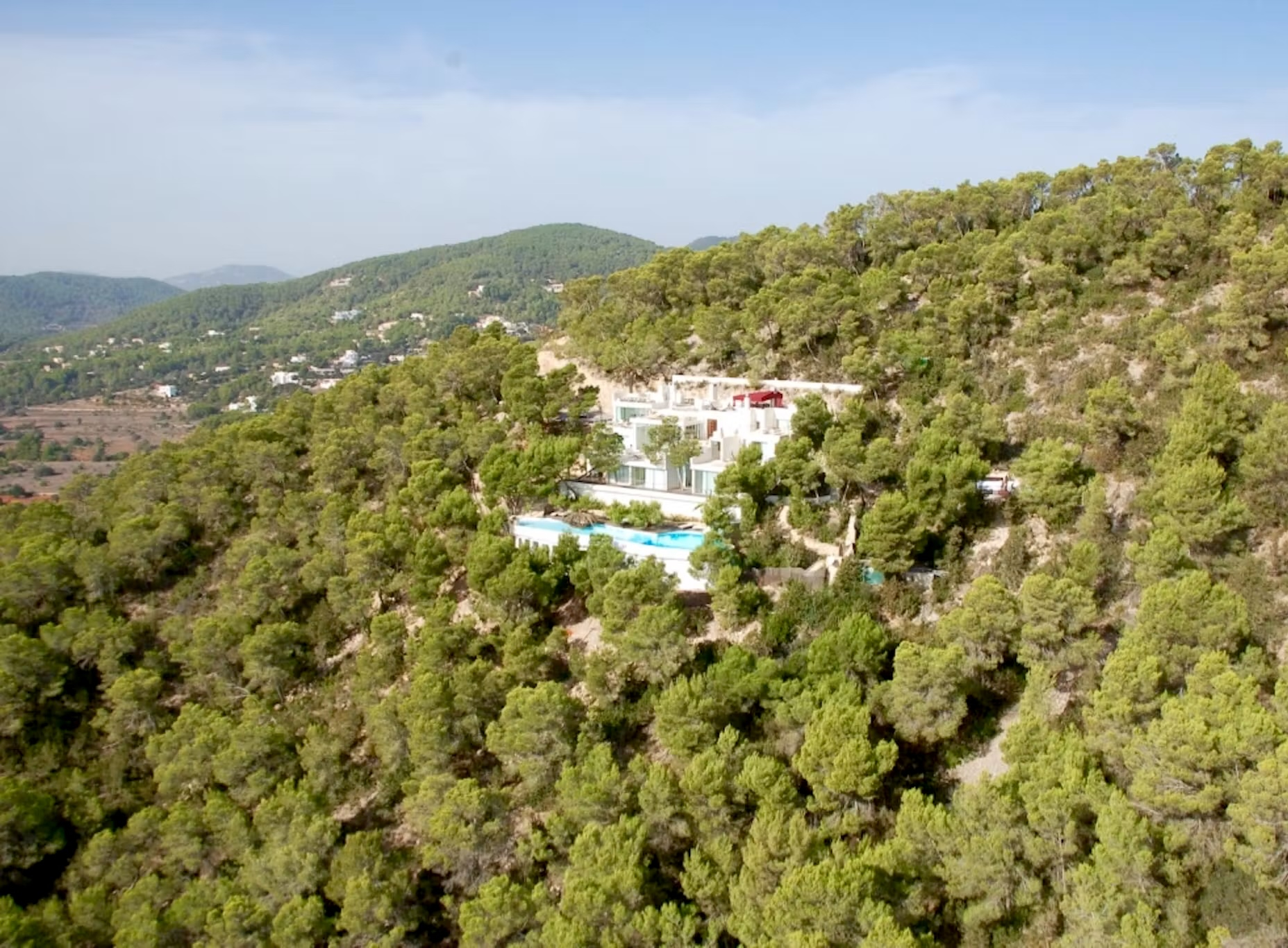 Wide aerial view of Villa Destiny Ibiza, with its white exterior and swimming pool set among trees on a hillside