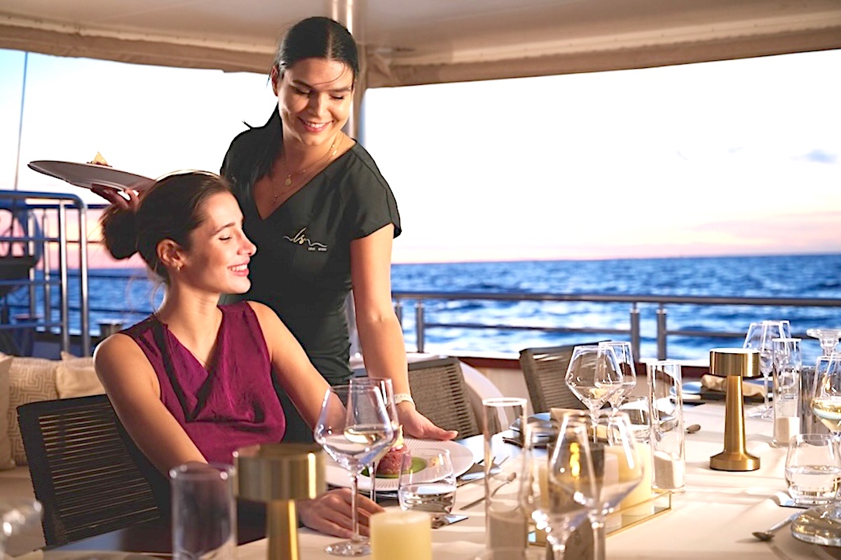 Crew member serving a guest during dinner aboard a private yacht