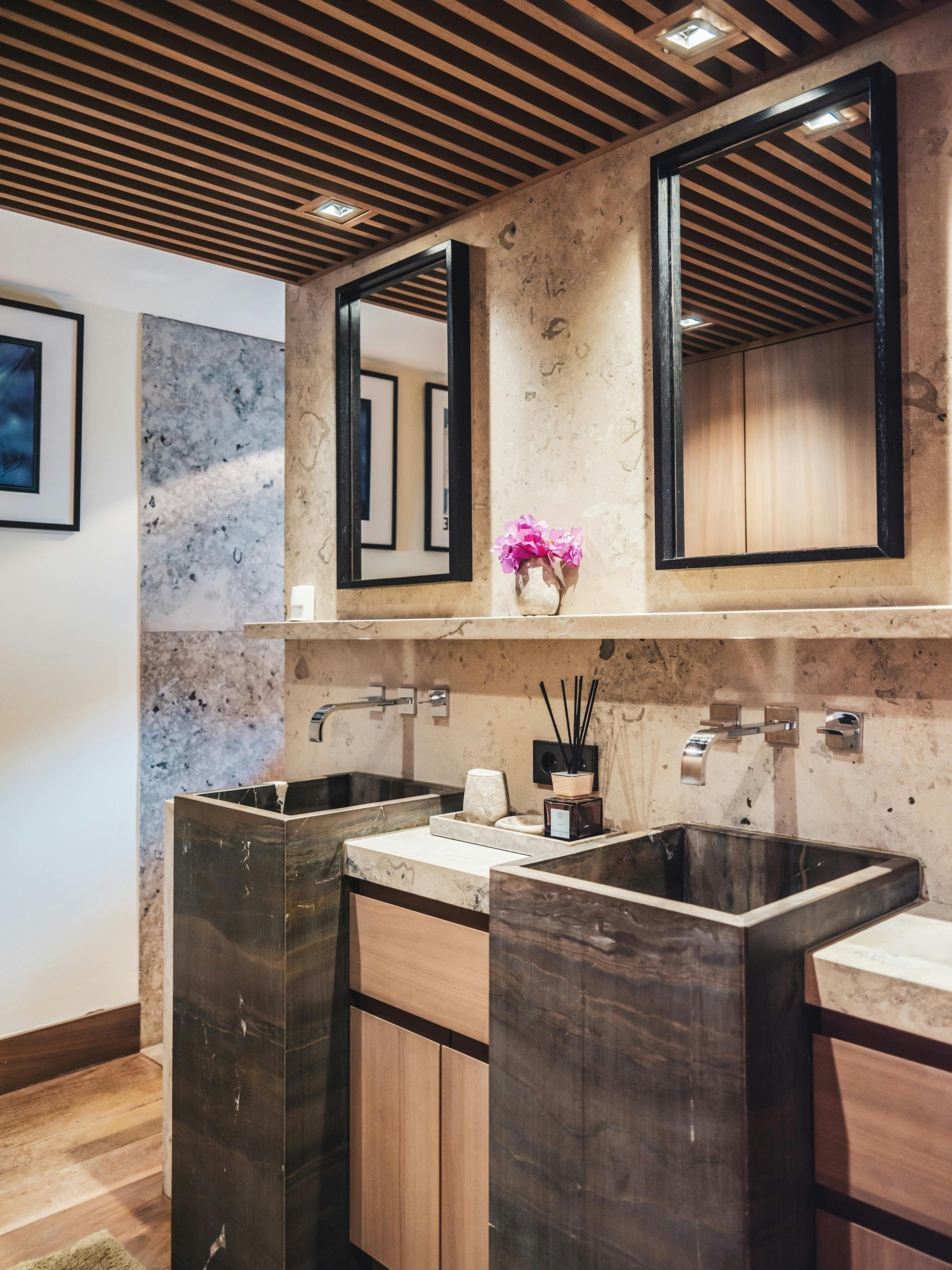 Twin dark stone basins with wall-mounted faucets and tall mirrors in a stone-clad bathroom at Ocean Paradise in Ibiza