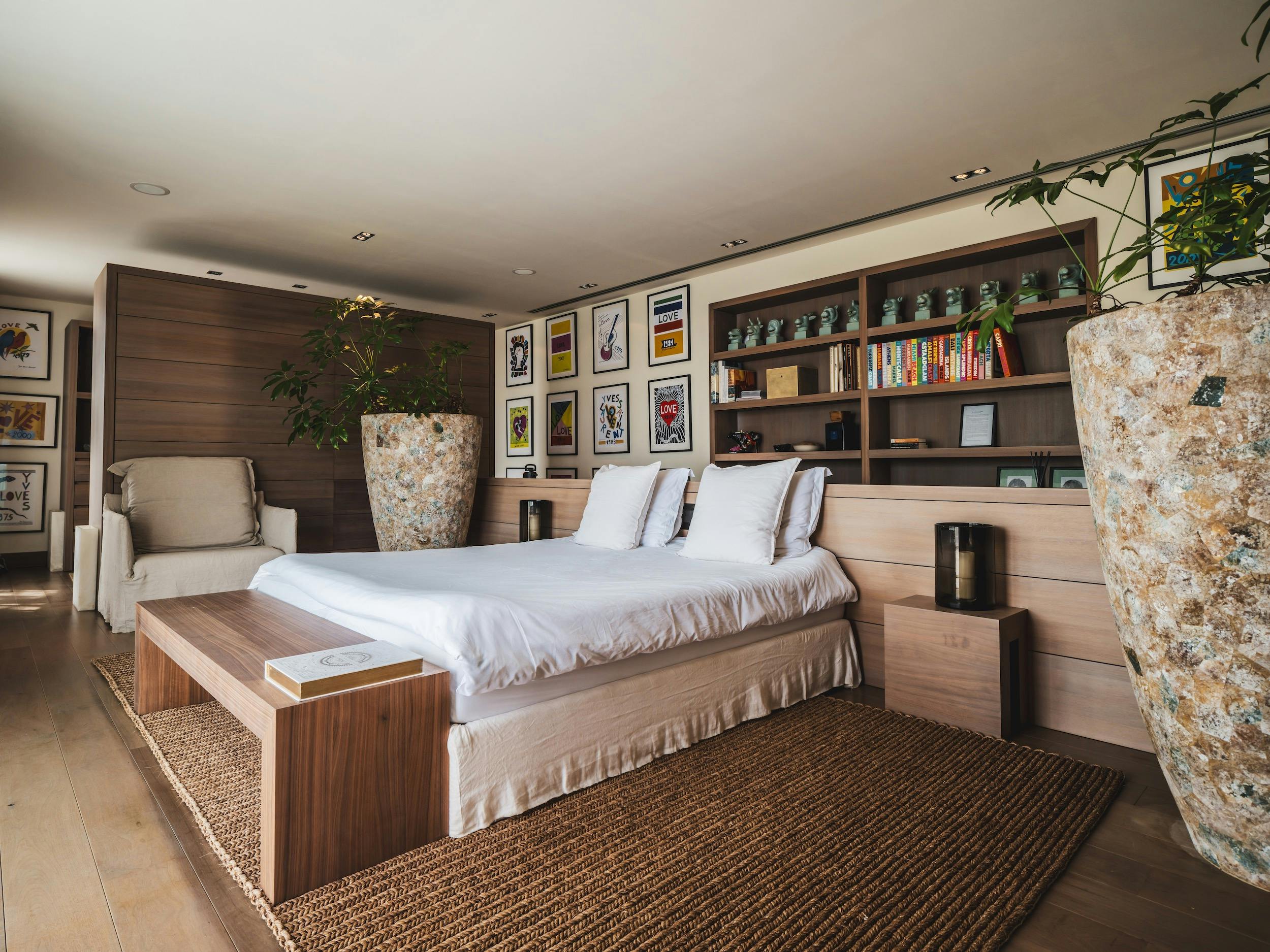 Bedroom with white bedding, wood furnishings, bookshelves, and colorful framed artwork at Ocean Paradise in Ibiza