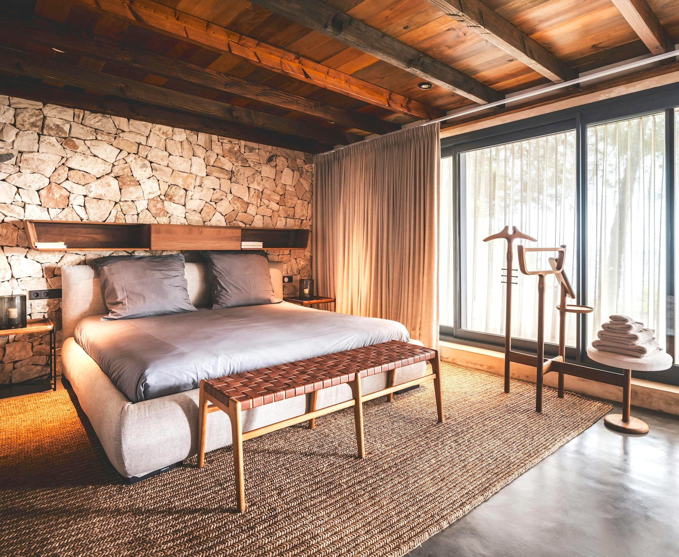 Bedroom at Ocean Paradise villa in Ibiza with a natural stone wall, wood ceiling, and full-height glass doors