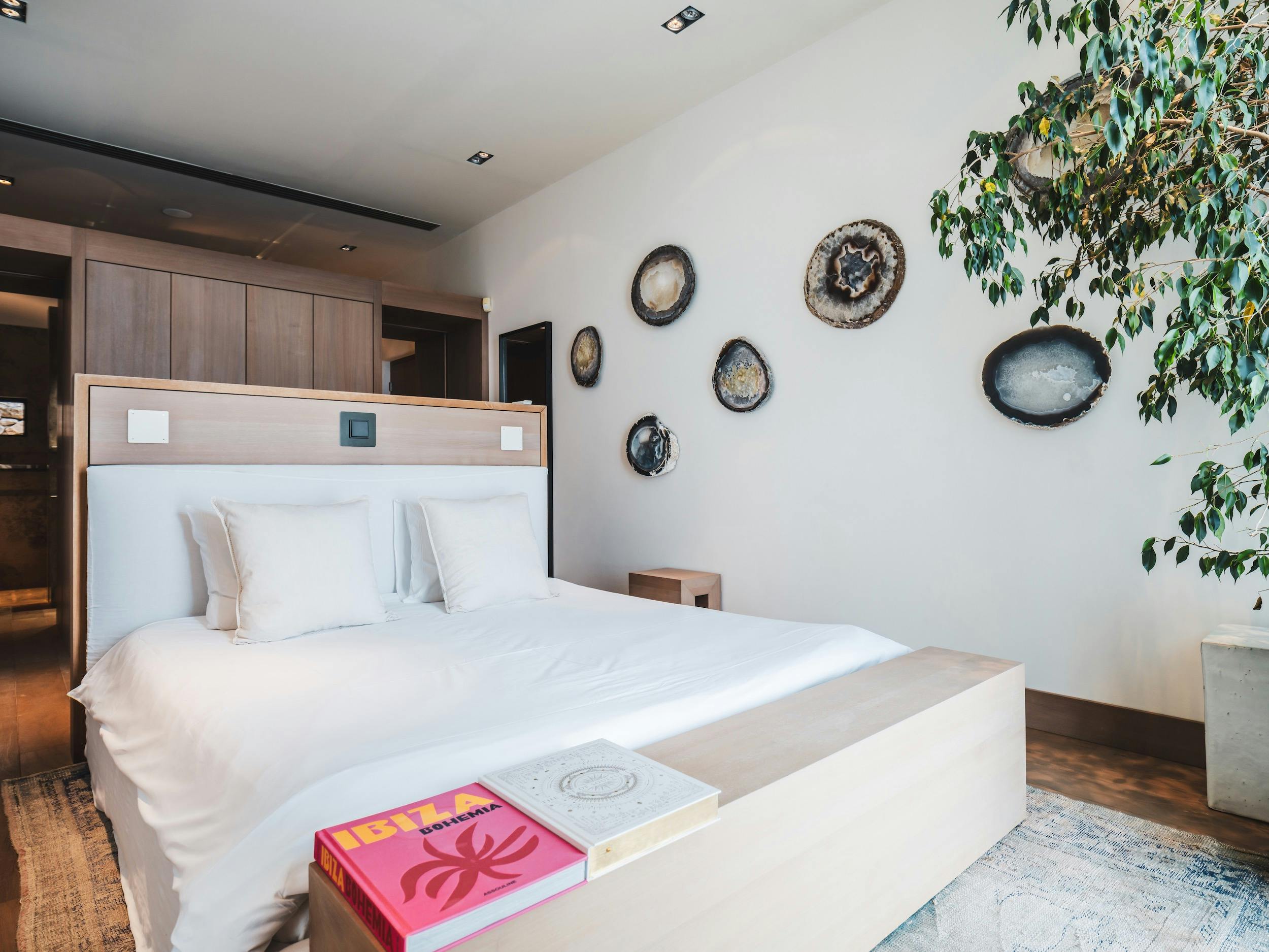 Bedroom with white bedding, a wood headboard, decorative stone discs, and an indoor tree at Ocean Paradise in Ibiza
