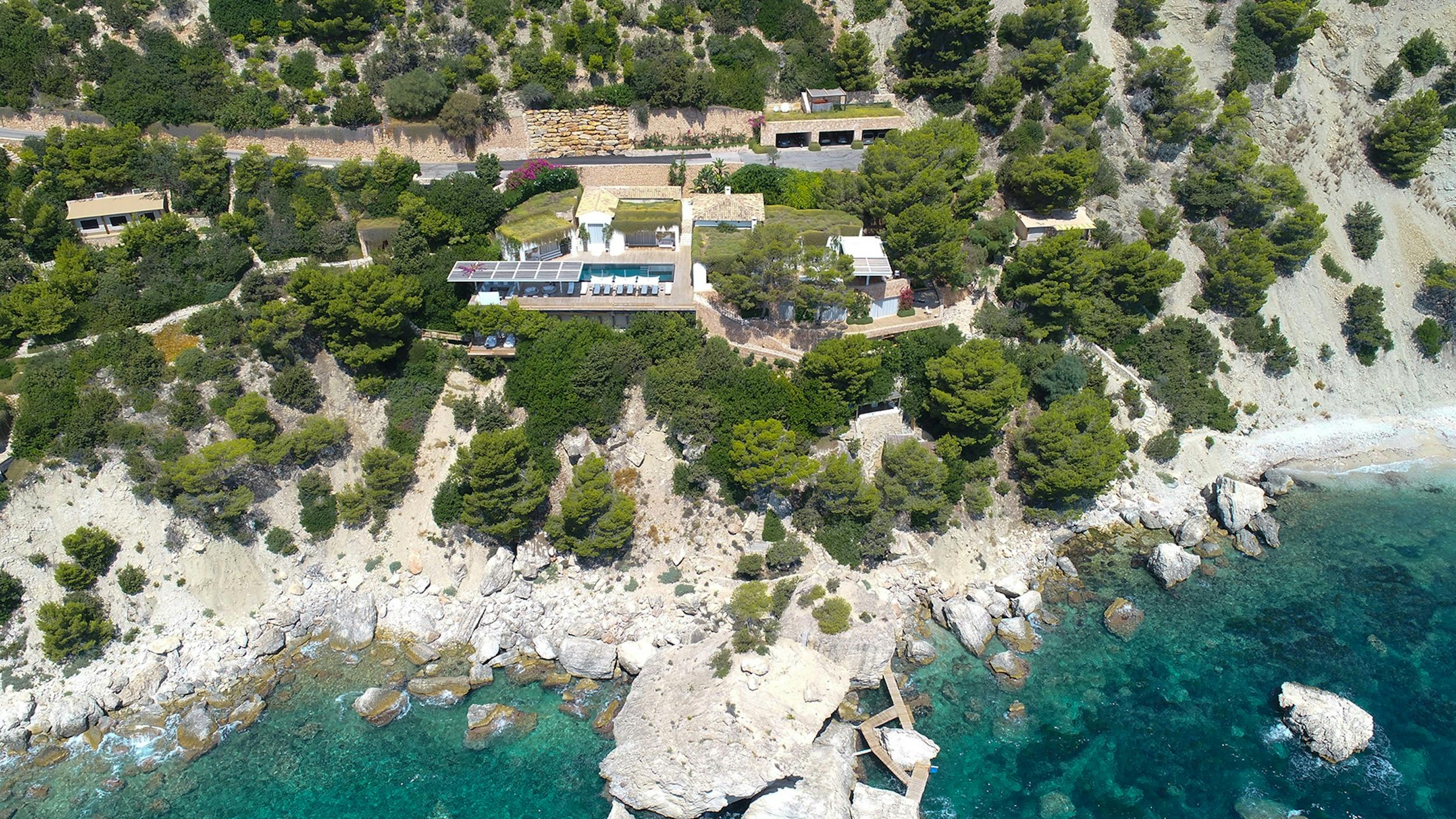 Aerial view of Ocean Paradise in Es Cubells, Ibiza, showing the villa, pool, terraced grounds, and rocky shoreline