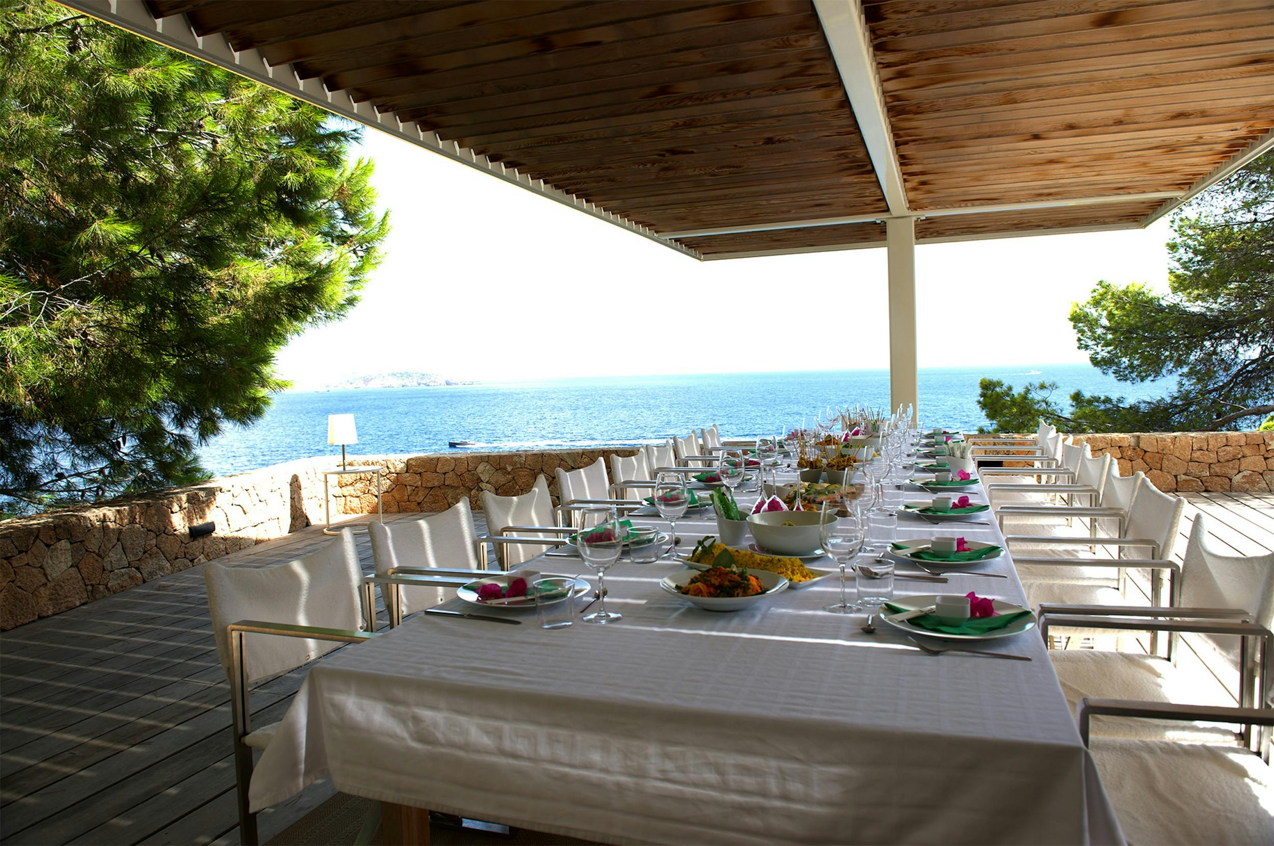 Long table set for a shared meal beneath a wooden terrace roof, overlooking the Mediterranean at Ocean Paradise in Ibiza