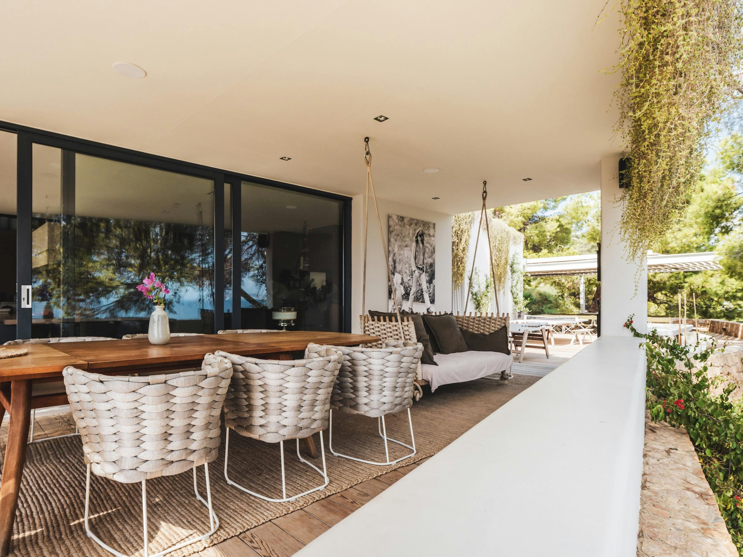 Covered terrace with a wooden table, woven chairs, and a suspended sofa beside sliding glass doors at Ocean Paradise in Ibiza