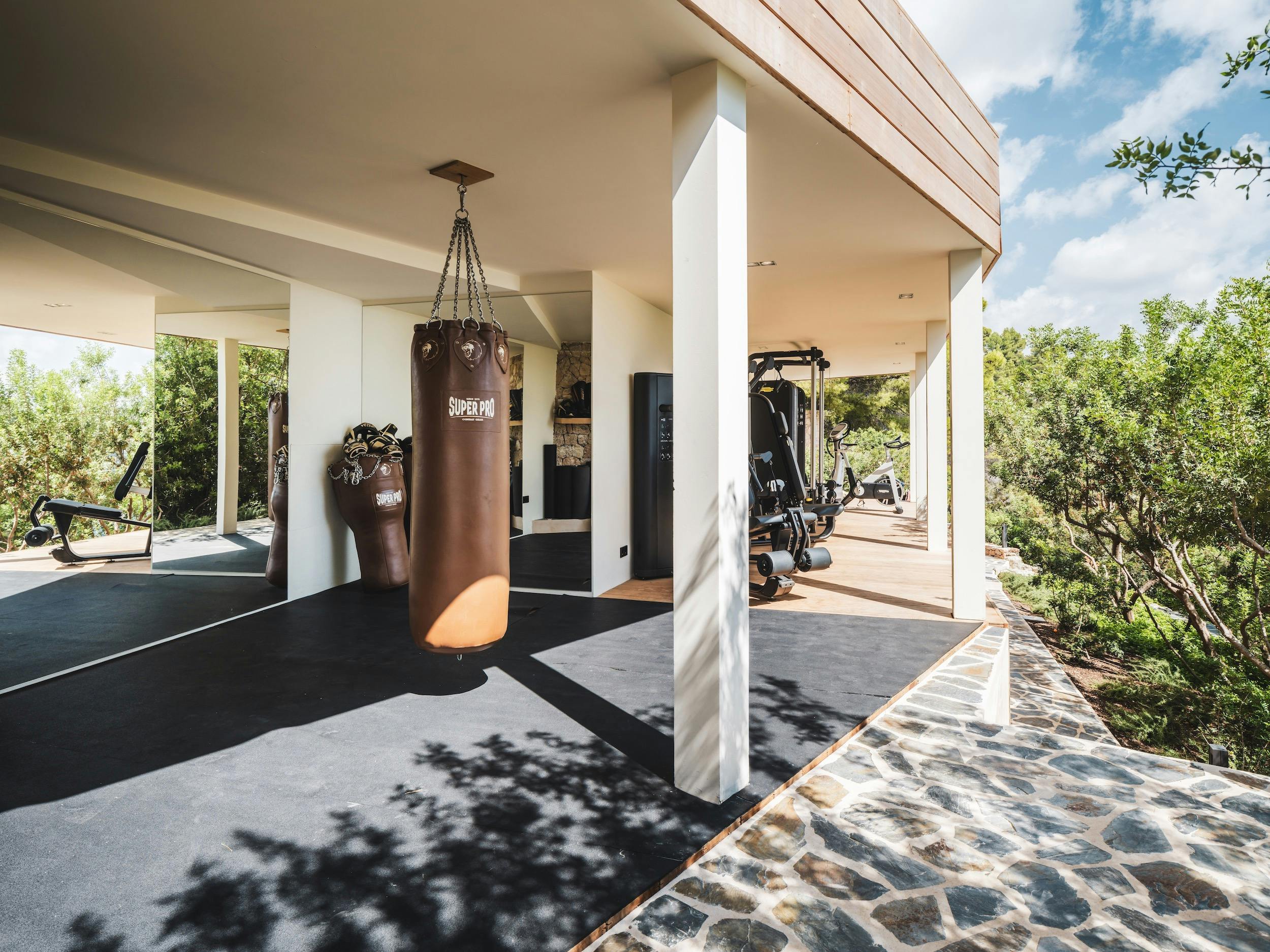 Open-sided gym with a punching bag, mirrored wall, strength equipment, and exercise bikes at Ocean Paradise in Ibiza