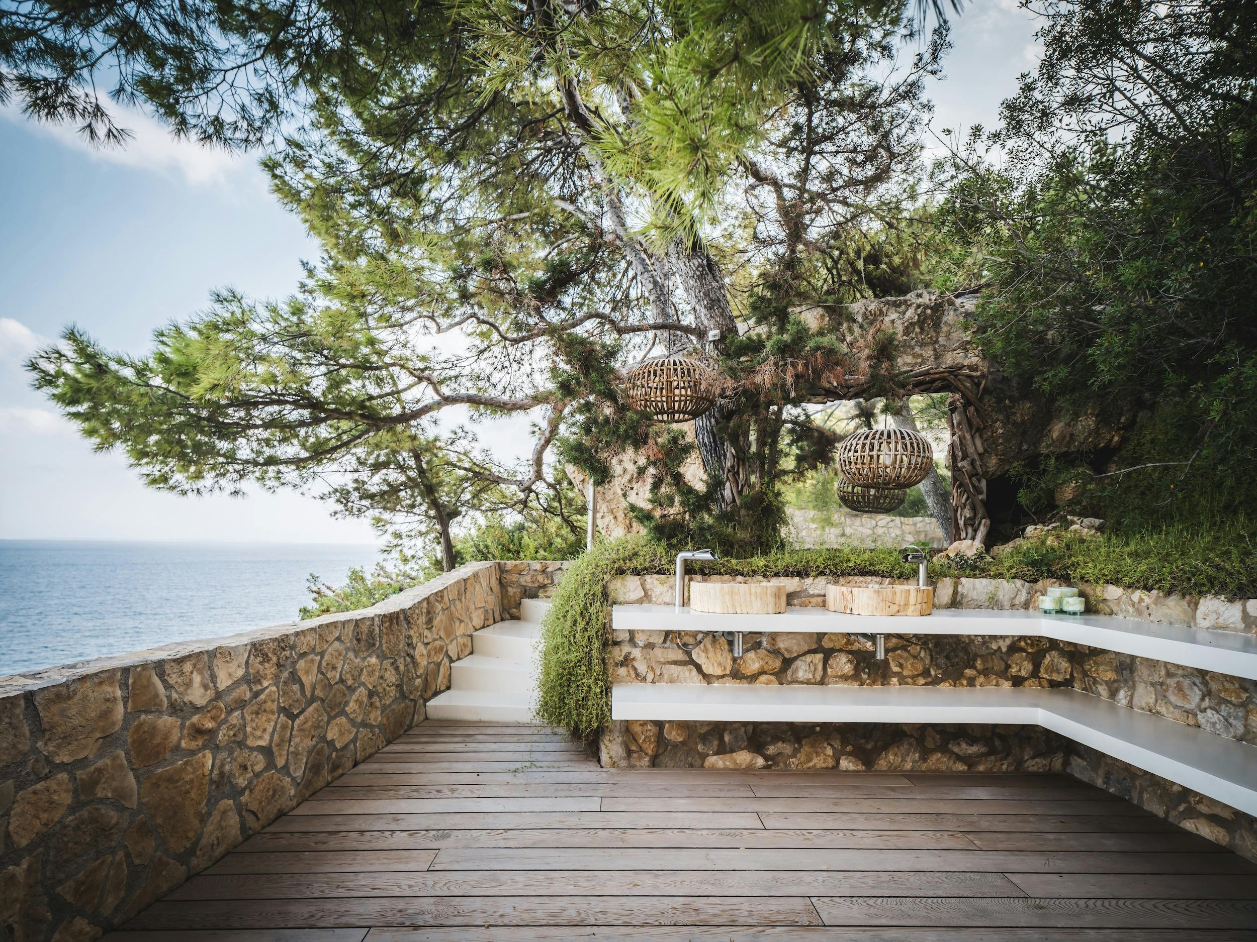 Twin outdoor washbasins with a rustic mirror, stone walls, and sea views at Ocean Paradise Ibiza