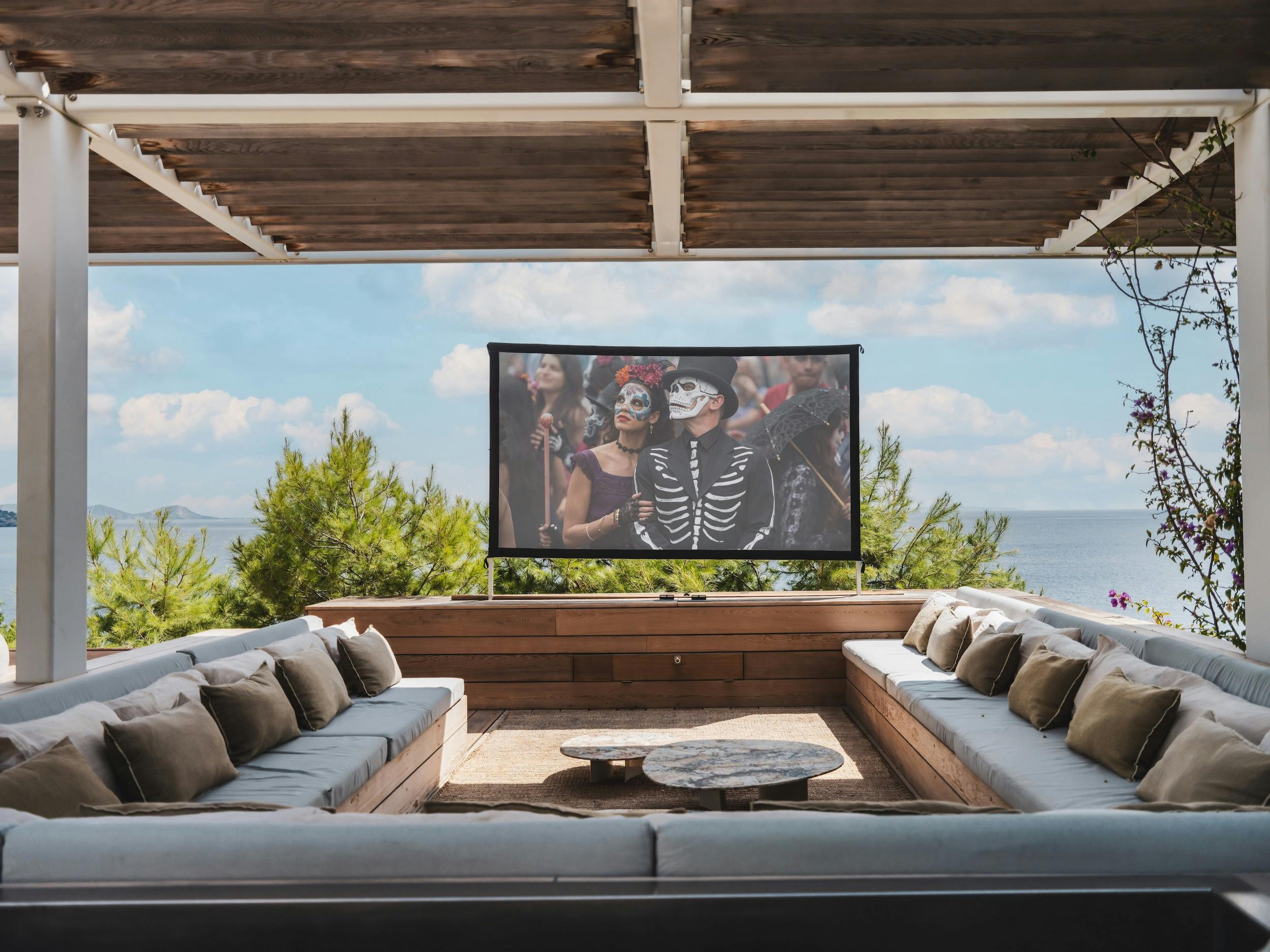 Covered lounge with wraparound cushioned seating and a cinema screen overlooking the Mediterranean at Ocean Paradise in Ibiza
